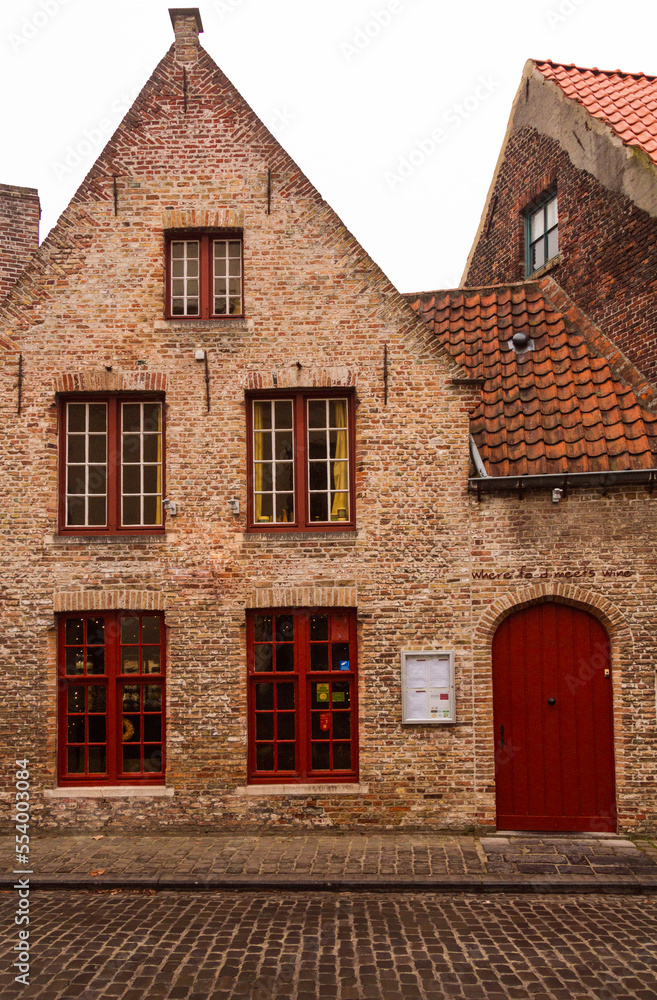 red windows and door on an old brick house in brugge, facade
