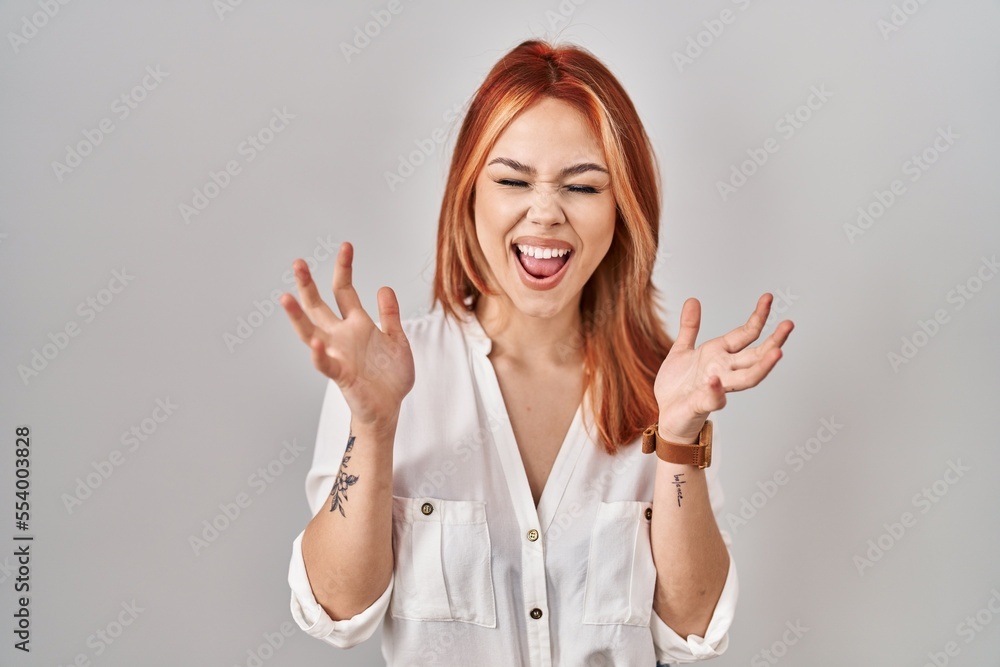 Young caucasian woman standing over isolated background celebrating mad and crazy for success with arms raised and closed eyes screaming excited. winner concept Young caucasian woman standing over isolated background celebrating mad and crazy for success with arms raised and closed eyes screaming excited. winner concept