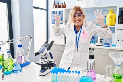 Middle age blonde woman working at scientist laboratory celebrating crazy and amazed for success with arms raised and open eyes screaming excited. winner concept