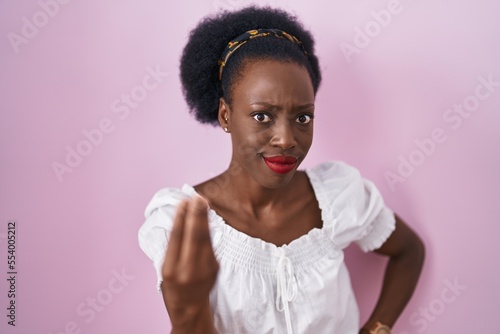 African woman with curly hair standing over pink background doing italian gesture with hand and fingers confident expression