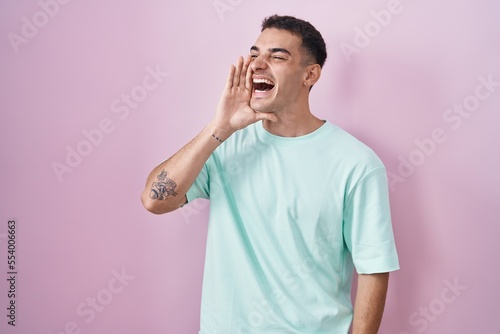 Handsome hispanic man standing over pink background shouting and screaming loud to side with hand on mouth. communication concept.