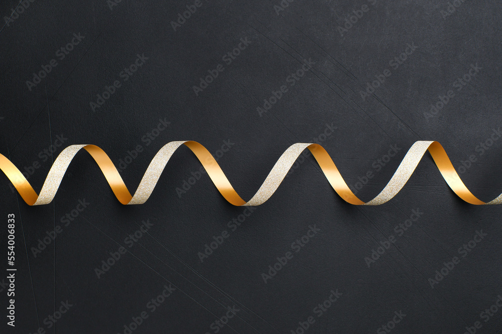 Festive background holiday decorations  golden shiny confetti in the form of stars and gold ribbon spiral serpentine on black background. Copy space