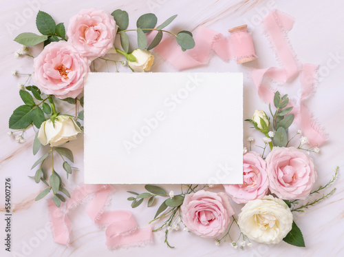 Blank paper card between pink roses and silk ribbons on marble top view, wedding mockup © katrinshine