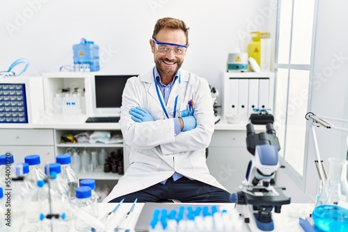 Middle age man working at scientist laboratory happy face smiling with crossed arms looking at the camera. positive person.