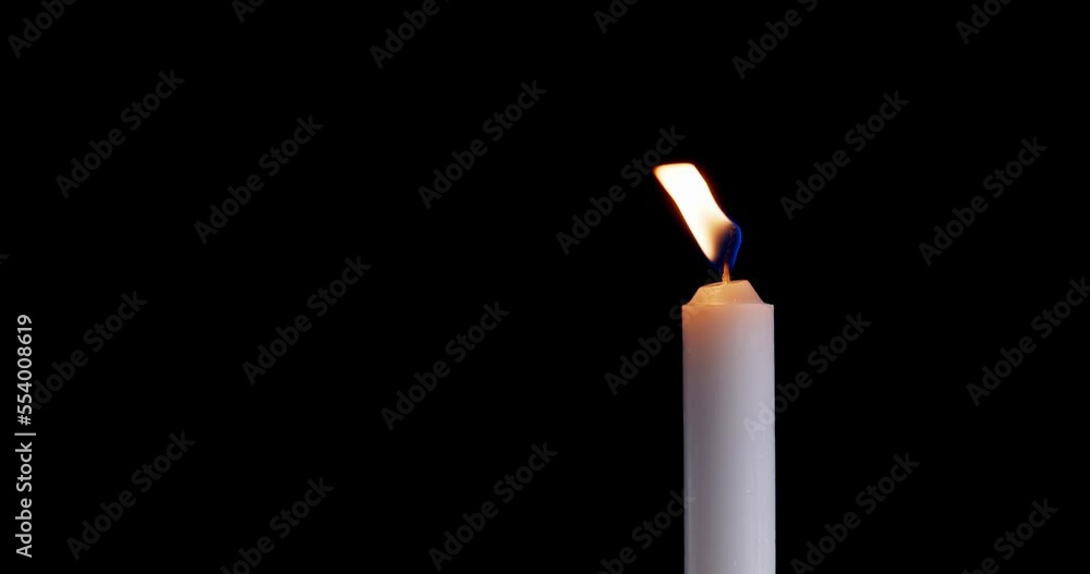 A single white candle burning. Isolated candle slow motion burning with dark background. White paraffin candle with yellow shades burns on a black background. Slow motion. A single white candle burning. Isolated candle slow motion burning with dark background. White paraffin candle with yellow shades burns on a black background. Slow motion.