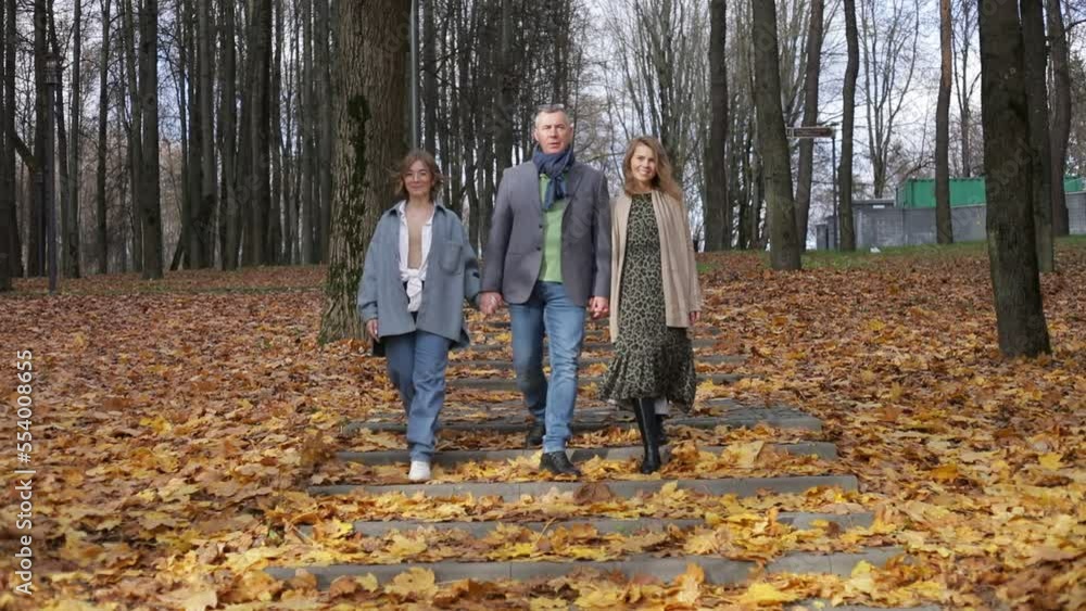 Happy family of three people go forward along steps with yellow leaves around in forest. Parents and teenage child walk in autumn park. Beautiful nature landscape, defoliation. Family rest, lifestyle Happy family of three people go forward along steps with yellow leaves around in forest. Parents and teenage child walk in autumn park. Beautiful nature landscape, defoliation. Family rest, lifestyle