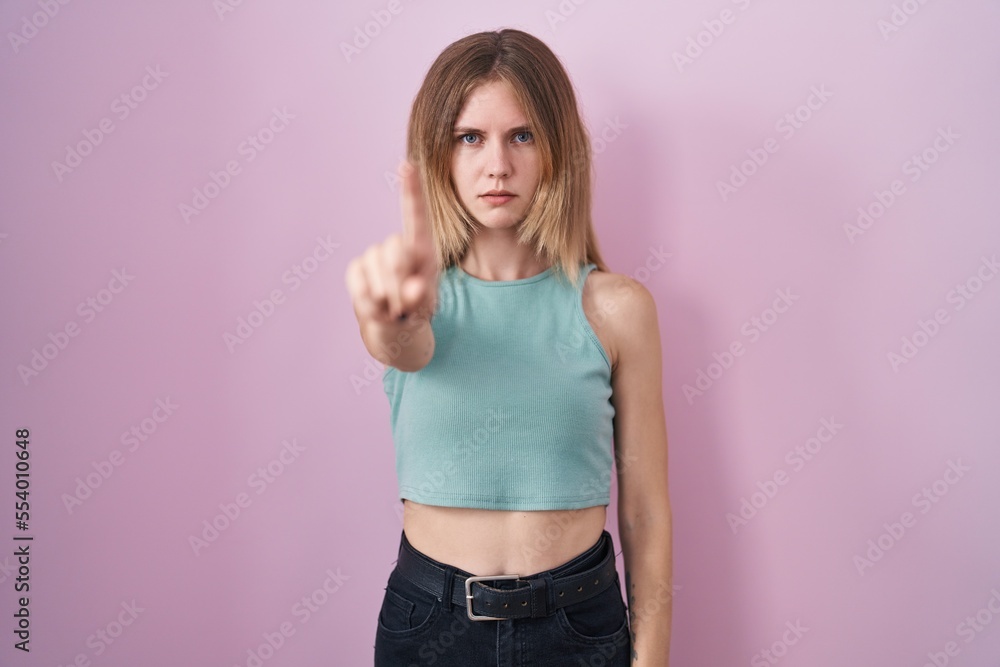 Blonde caucasian woman standing over pink background pointing with finger up and angry expression, showing no gesture Blonde caucasian woman standing over pink background pointing with finger up and angry expression, showing no gesture