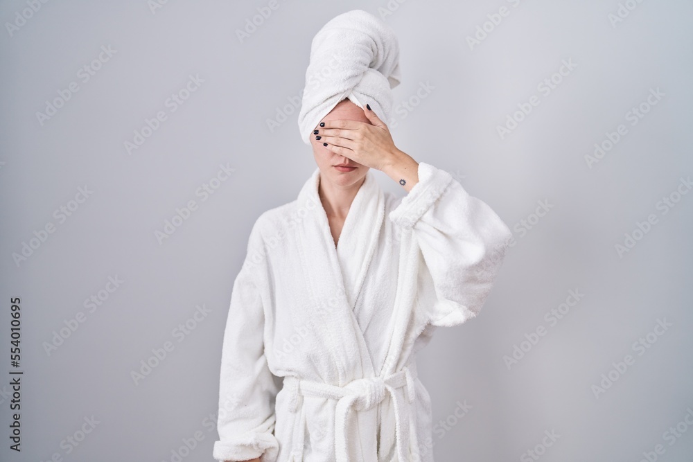 Blonde caucasian woman wearing bathrobe covering eyes with hand, looking serious and sad. sightless, hiding and rejection concept Blonde caucasian woman wearing bathrobe covering eyes with hand, looking serious and sad. sightless, hiding and rejection concept