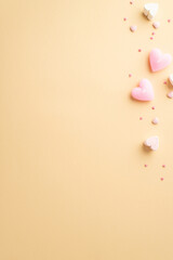 St Valentine's Day concept. Top view vertical photo of heart shaped candles marshmallow and sprinkles on isolated light beige background with copyspace