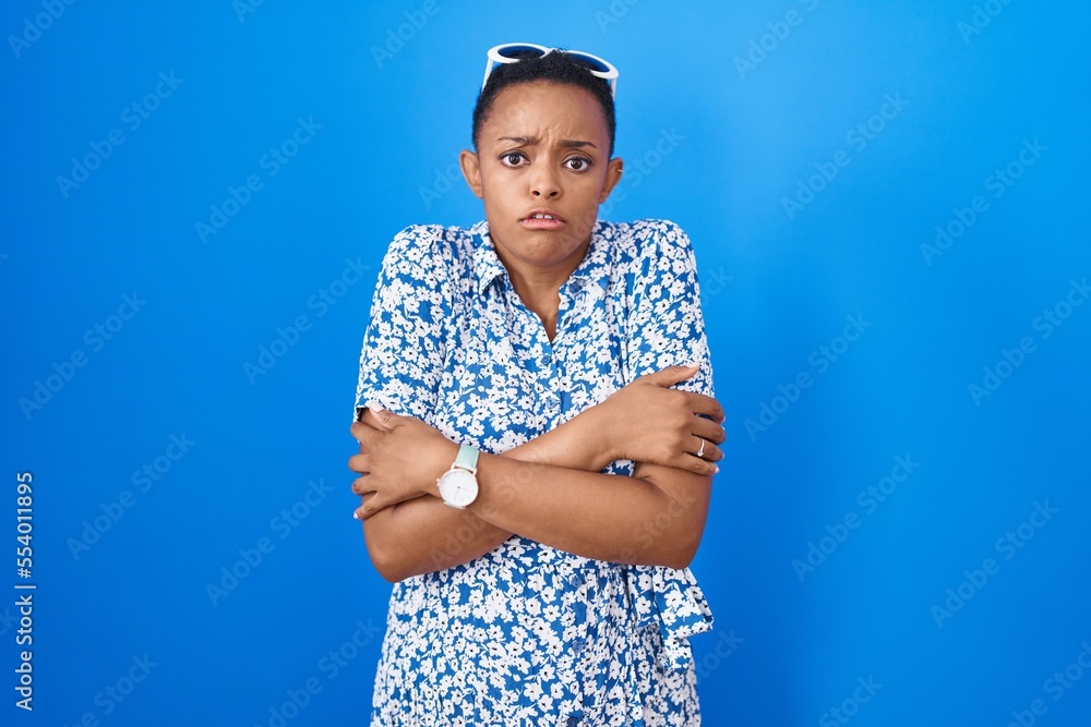 African american woman standing over blue background shaking and freezing for winter cold with sad and shock expression on face
