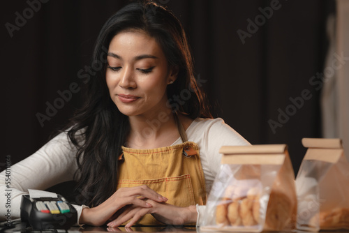 Bakery and coffee cafe business shop concept, Asian female wearing aprons, happily smiling to serving breakfast baked bread, beautiful woman staff service customer to delivery a food