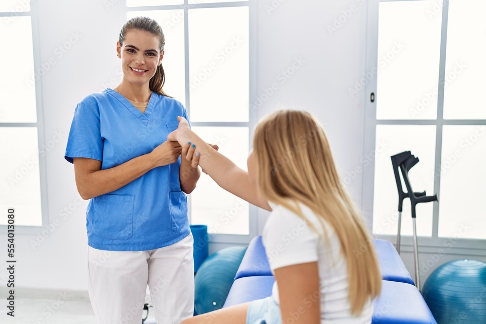 Obraz premium Woman and girl physiotherapist and patient having rehab session stretching hand at physiotherapy clinic
