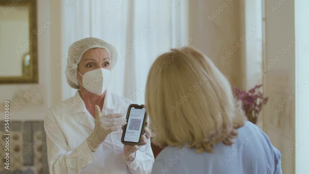 Cheerful doctor showing senior woman qr code of vaccinated. Slow motion of female therapist explaining patient where to find qr code after vaccination at home. Immunization, technology concept Cheerful doctor showing senior woman qr code of vaccinated. Slow motion of female therapist explaining patient where to find qr code after vaccination at home. Immunization, technology concept