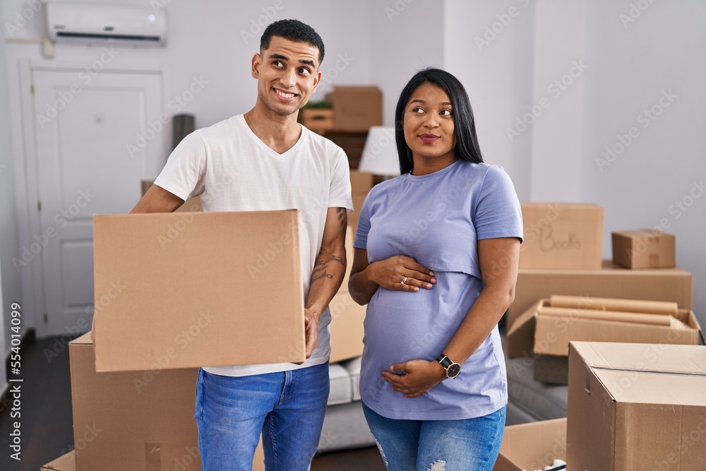 Young hispanic couple expecting a baby moving to a new home smiling looking to the side and staring away thinking. Young hispanic couple expecting a baby moving to a new home smiling looking to the side and staring away thinking.
