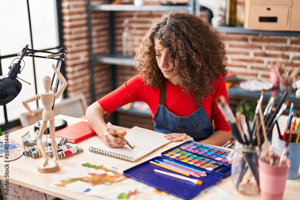 Fototapeta premium Young hispanic woman artist drawing on notebook at art studio