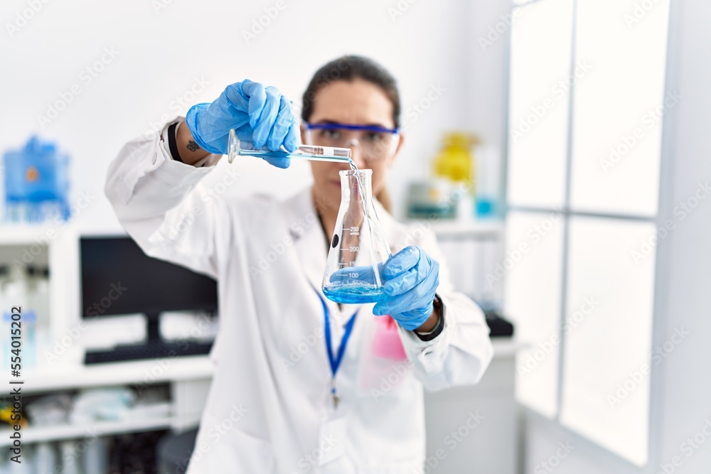 Naklejka premium Young hispanic woman wearing scientist uniform holding test tube at laboratory