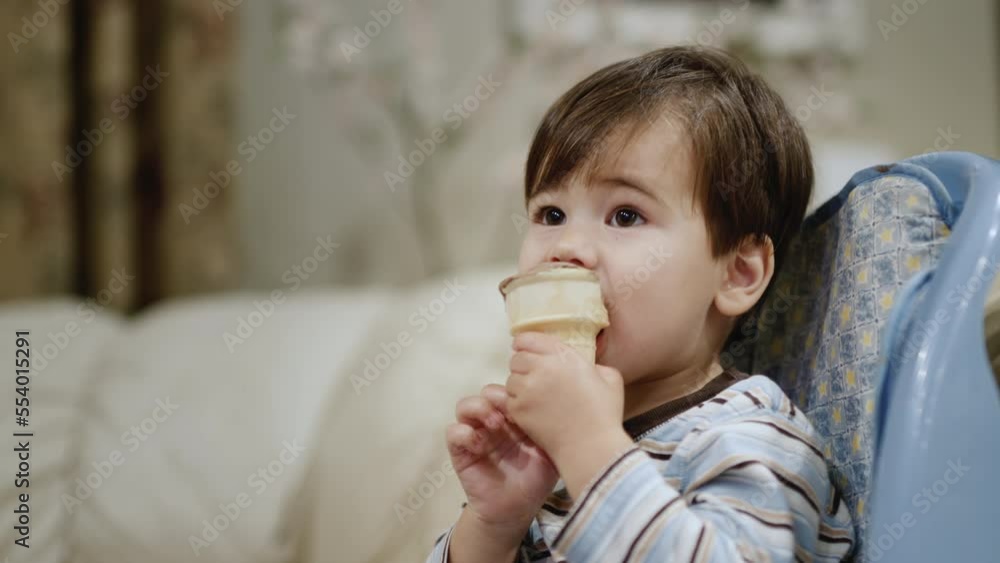 Two years old Asian baby eats ice cream, sits in a child seat for feeding. Side view Two years old Asian baby eats ice cream, sits in a child seat for feeding. Side view