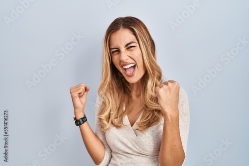 Young blonde woman standing over isolated background very happy and excited doing winner gesture with arms raised, smiling and screaming for success. celebration concept.