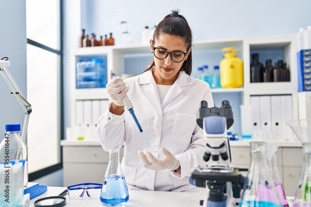 Young hispanic woman wearing scientist uniform using pipette working at laboratory Young hispanic woman wearing scientist uniform using pipette working at laboratory