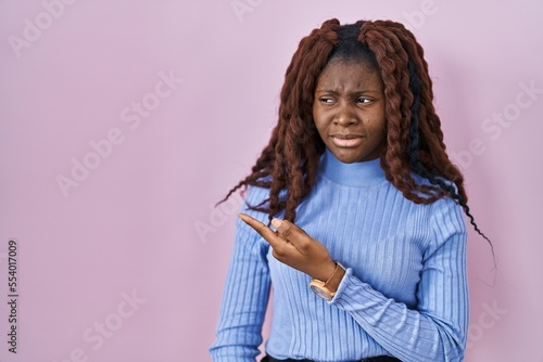 African woman standing over pink background pointing aside worried and nervous with forefinger, concerned and surprised expression