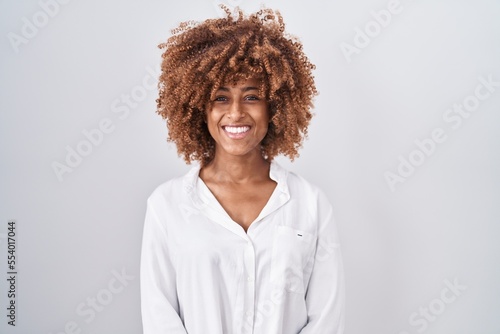 Young hispanic woman with curly hair standing over white background with a happy and cool smile on face. lucky person.