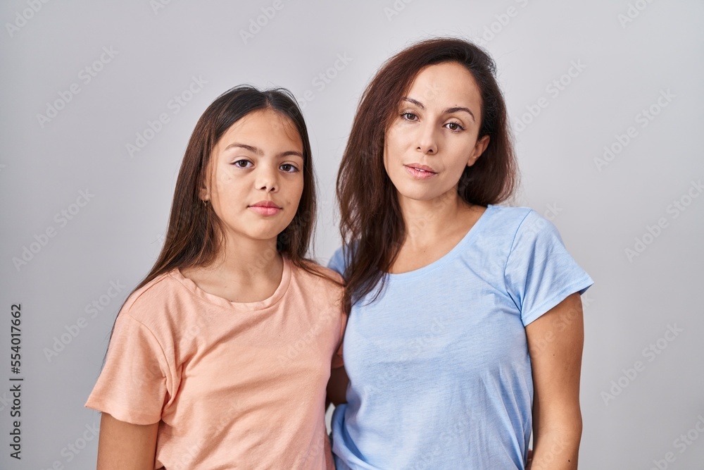 Young mother and daughter standing over white background relaxed with serious expression on face. simple and natural looking at the camera. Young mother and daughter standing over white background relaxed with serious expression on face. simple and natural looking at the camera.