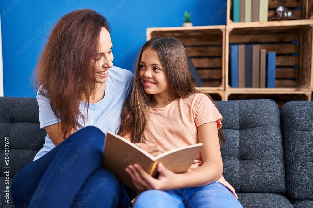 Woman and girl mother and daughter reading book at home Woman and girl mother and daughter reading book at home