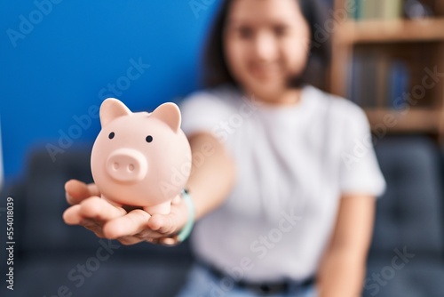 Young woman holding piggy bank sitting on sofa at home