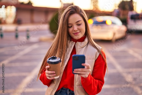 Young blonde woman using smartphone drinking coffee at street