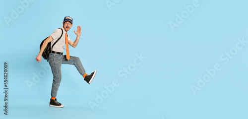 Portrait of young man, student in casual clothes cheerfully walking isolated over blue background