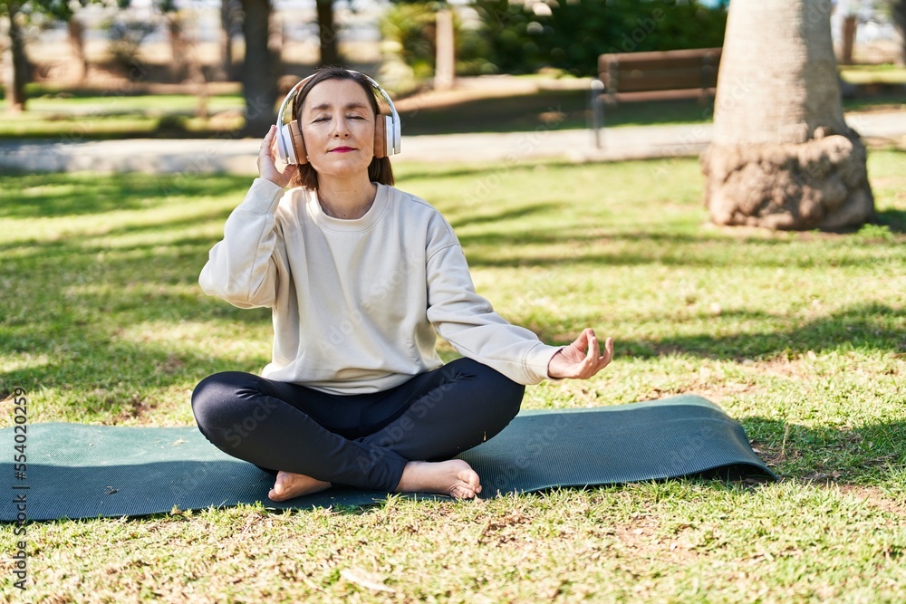 Middle age woman doing yoga exercise sitting on herb at park Middle age woman doing yoga exercise sitting on herb at park