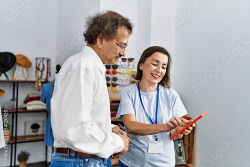 Middle age man and woman smiling confident choosing clothes using touchpad at clothing store