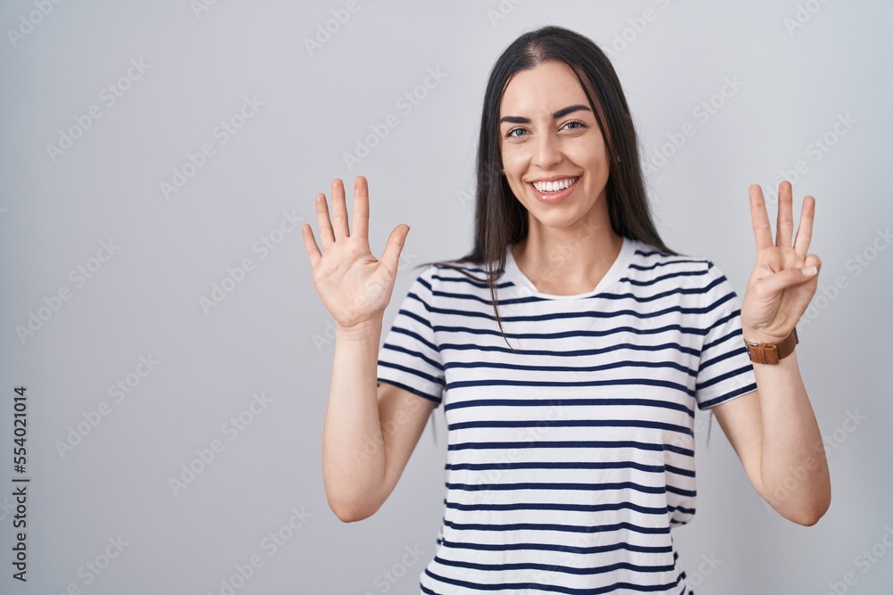 Young brunette woman wearing striped t shirt showing and pointing up with fingers number eight while smiling confident and happy. Young brunette woman wearing striped t shirt showing and pointing up with fingers number eight while smiling confident and happy.