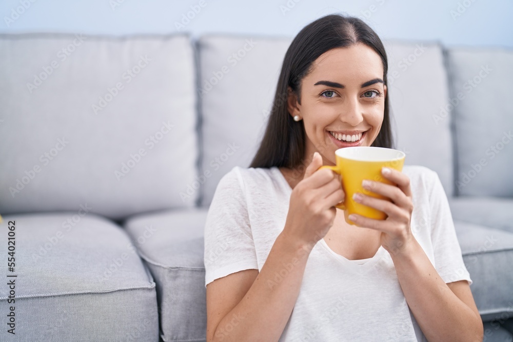 Young hispanic woman drinking coffee sitting on floor at home Young hispanic woman drinking coffee sitting on floor at home