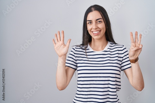 Young brunette woman wearing striped t shirt showing and pointing up with fingers number eight while smiling confident and happy.