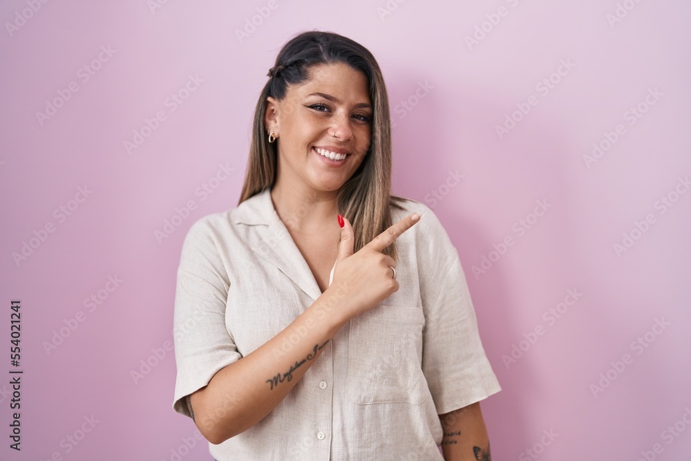 Blonde woman standing over pink background cheerful with a smile on face pointing with hand and finger up to the side with happy and natural expression Blonde woman standing over pink background cheerful with a smile on face pointing with hand and finger up to the side with happy and natural expression