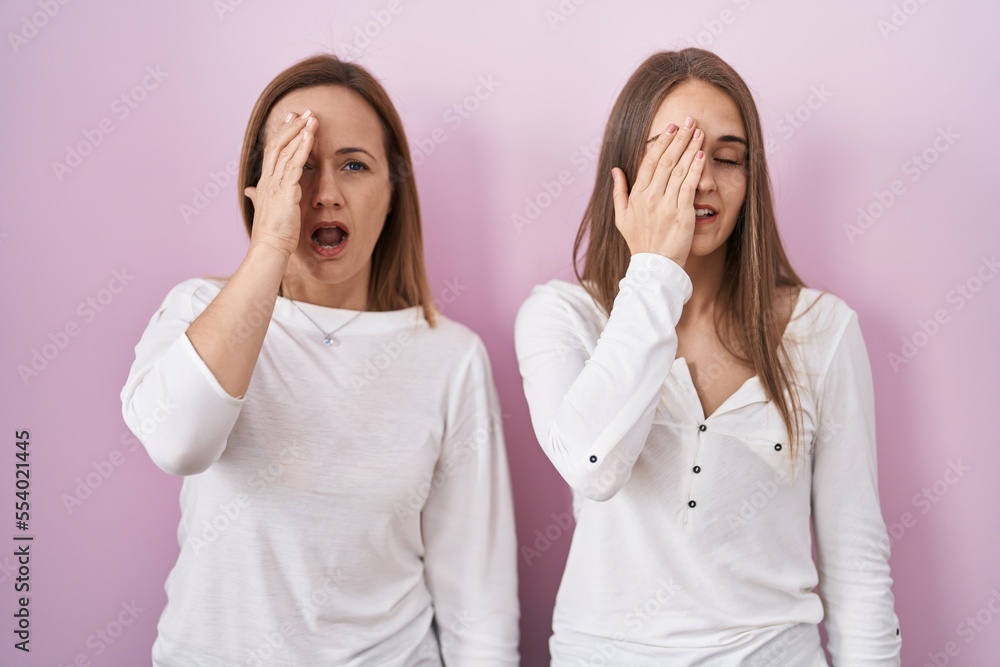 Middle age mother and young daughter standing over pink background yawning tired covering half face, eye and mouth with hand. face hurts in pain. Middle age mother and young daughter standing over pink background yawning tired covering half face, eye and mouth with hand. face hurts in pain.