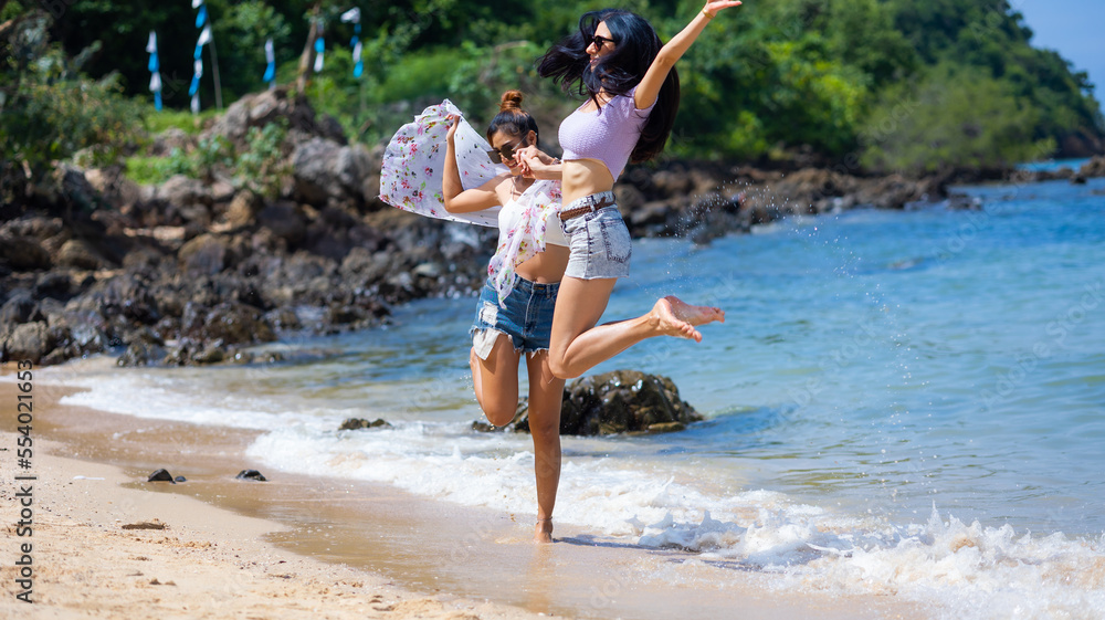 Naklejka premium Two Beautiful young women happy jumping together on the beach. Vacation trip summer holiday. friends holding hands jump enjoy life Vacation trip summer holiday.
