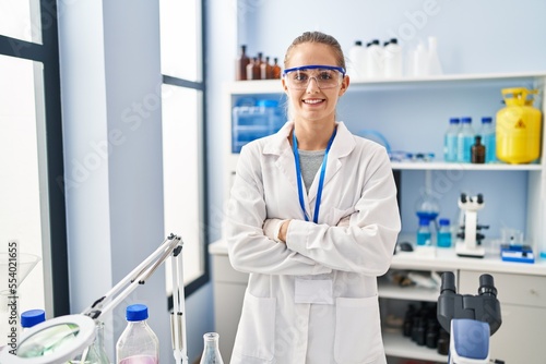 Young blonde woman wearing scientist uniform standing with arms crossed gesture at laboratory