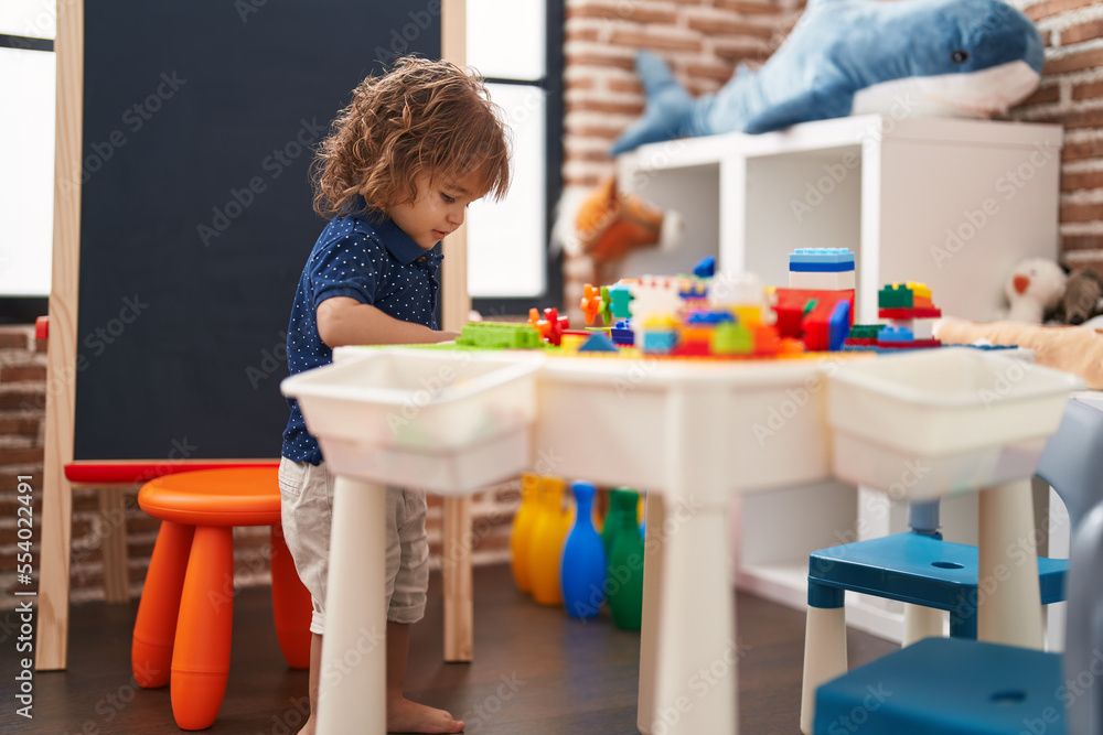 Adorable hispanic toddler playing with construction blocks standing at kindergarten Adorable hispanic toddler playing with construction blocks standing at kindergarten
