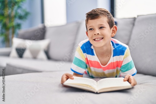 Blond child reading book sitting on sofa at home