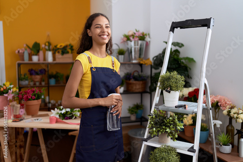 Young african american woman florist using diffuser watering plant at flower shop