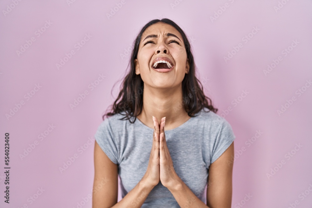 Young brazilian woman wearing casual t shirt over pink background begging and praying with hands together with hope expression on face very emotional and worried. begging. Young brazilian woman wearing casual t shirt over pink background begging and praying with hands together with hope expression on face very emotional and worried. begging.
