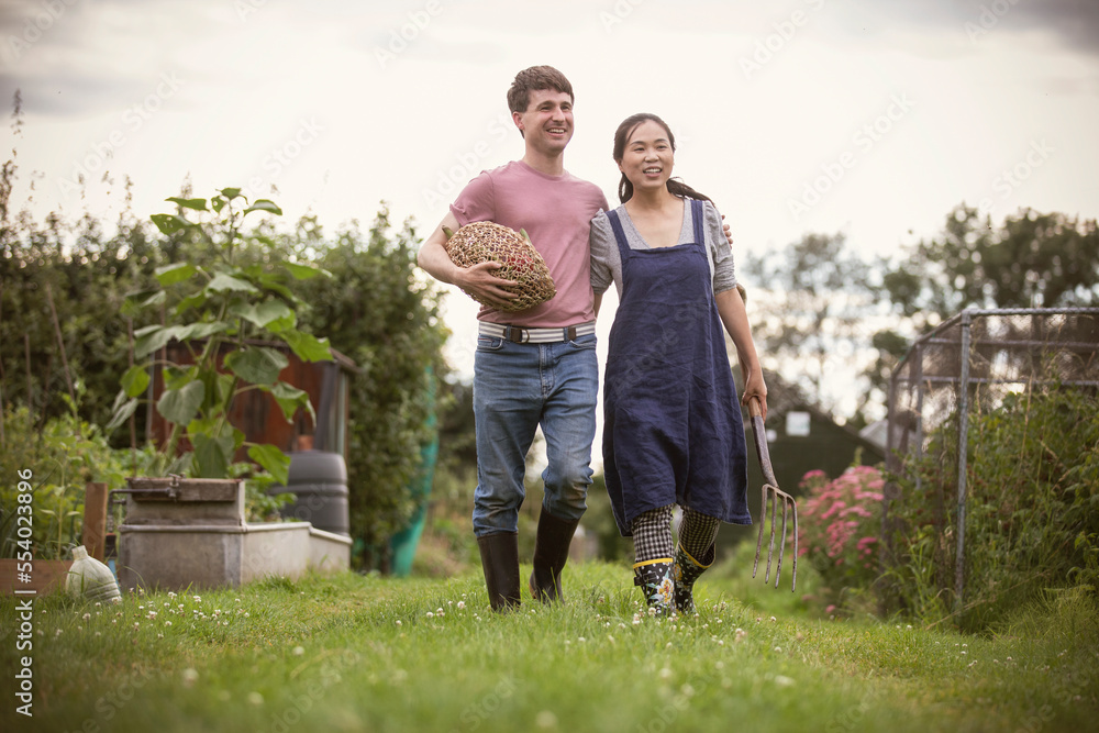 Happy couple walking with vegetables and pitchfork in garden Happy couple walking with vegetables and pitchfork in garden