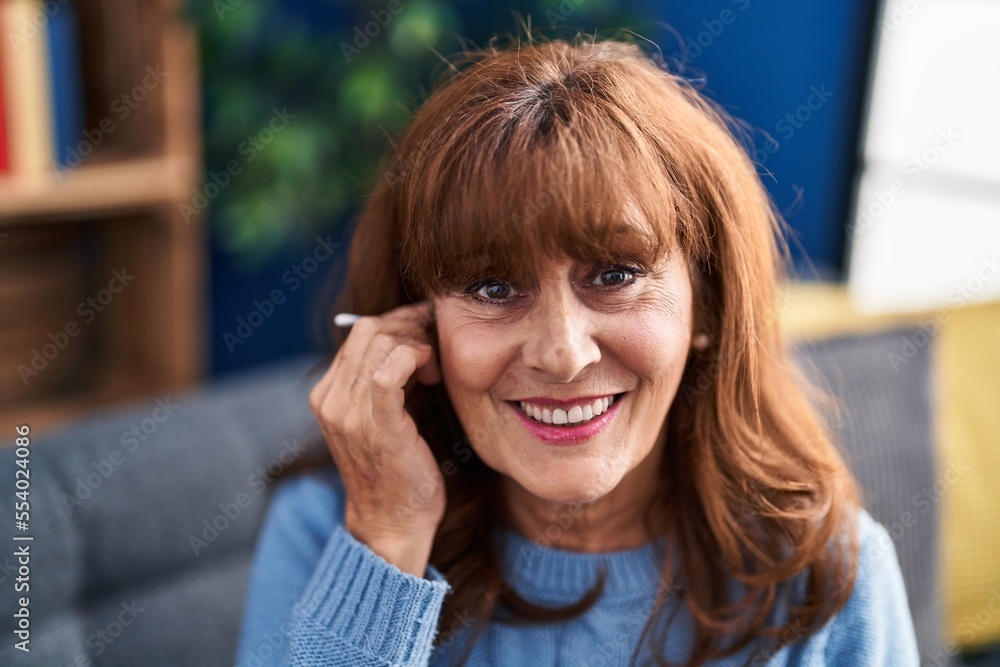Middle age woman clean¡ng ear sitting on sofa at home Middle age woman clean¡ng ear sitting on sofa at home