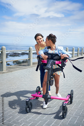 Mother and disabled daughter with rollator walking on sunny boardwalk