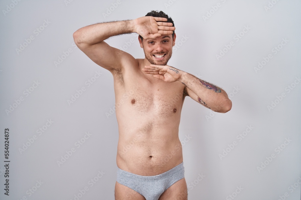 Fototapeta premium Young hispanic man standing shirtless wearing underware smiling cheerful playing peek a boo with hands showing face. surprised and exited