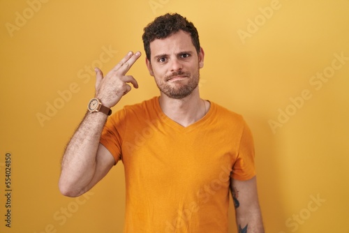 Canvas Print Young hispanic man standing over yellow background shooting and killing oneself pointing hand and fingers to head like gun, suicide gesture