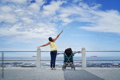 Mother and disabled daughter in pushchair stretching arms at ocean photo