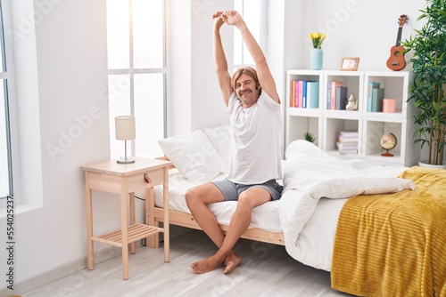 Young blond man waking up stretching arms at bedroom